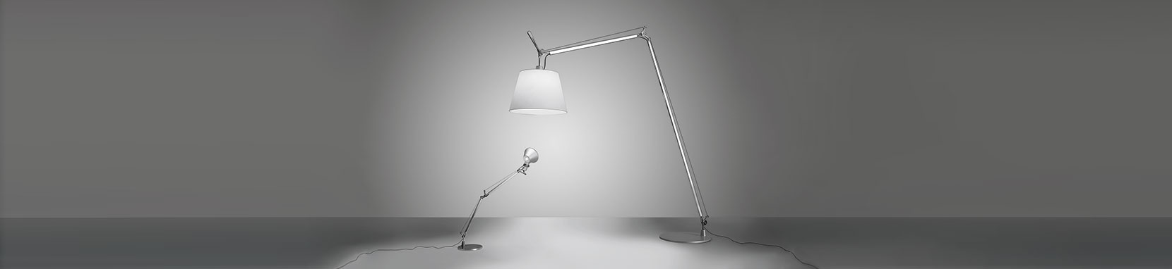 Die Tolomeo Mega Terra basiert auf der Artemide Tolomeo Tavolo, der wohl bekanntesten Schreibtischleuchte, die der Feder von Michele de Lucchi entstammt. Bereits 1987 wurde dieser Designklassiker zeitgemäßer Schreibtischbeleuchtung auf den Markt gebracht. Die Tolomeo Mega Terra Reihe wurde 2004 von Artemide in die Tolomeo Familie aufgenommen und sorgt für optimal zoniertes Leselicht neben Sofa und Sessel. Neben ihrem direkten Leselicht gibt die Tolomeo Mega Terra auch ein indirektes Raumlicht ab und ermöglicht somit ein atmosphärisches Leseambiente. Ihre gigantische Ausladung ermöglicht einen flexiblen und weiträumigen Einsatz. Die Mega Terra 42 ist mit einem 42 cm Leuchtenschirm ausgestattet, den es in den Oberflächen Stoff Natur und Stoff grau gibt, die Leuchtenbasis ist aus poliertem Aluminium und die Leuchte verfügt über einen stufenlosen Dimmer. Erhältlich ist die Mega Terra Serie auch mit 32er und 36er Schirm. Die Leuchtenserie Tolomeo überzeugt mit ihren technischen Eigenschaften und dem komfortabel ausrichtbaren sowie blendfreien Licht. Tolomeo steht für erstklassige Verarbeitung, maximale Flexibilität, beste Lichtqualität und einen enormen Einsatzradius. Dank dieser hervorragenden Eigenschaften und dem zeitlosen Design wurde die Tolomeo zu der vielleicht weltweit verbreitetsten Leuchte im Arbeitsplatzbereich überhaupt und fungiert bereits als Sinnbild für die italienische Designleuchtenfirma Artemide. Michele de Lucchi wurde für diese Leuchte mit internationalen Designpreisen überhäuft und die immer noch andauernde Erfolgsgeschichte der Tolomeo macht dieses Meisterstück unweigerlich zum Lebenswerk des Stardesigners. Das beeindruckende Portfolio der Tolomeo Familie erstreckt sich von der klassischen Schreibtischleuchte über Stehleuchten, Wandleuchten bis hin zu Decken- oder Pendelleuchten und wartet mit verschiedensten Oberflächen und Werkstoffen auf.